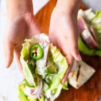 A hand holding a lettuce with the tuna, veggies and sauce drizzled on top.