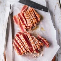 A sharp knife on a cutting board slicing the tuna super thin , showing how pink the tuna is on the inside and the beautiful crust