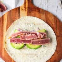 Some veggies piled over the tortilla along the middle including avocados, onions, cucumbers, carrots, and the sliced tuna on top