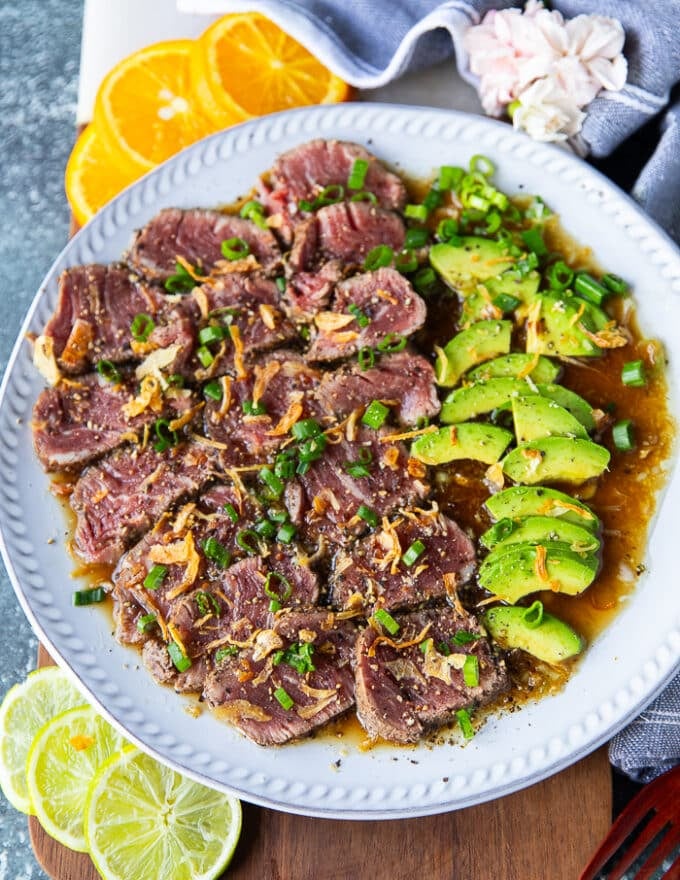 beef tataki recipe on a wooden board surrounded by lime slices and orange slices