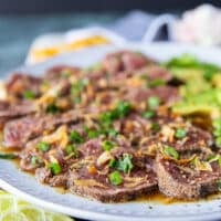 slices of beef and avocados added over the ponzu sauce and a hand sprinkling green onions and fried onions on top to finish the beef tataki