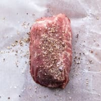 A piece of filet mignon or tenderloin seasoned with salt and pepper on parchment paper