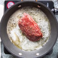 the seasoned tenderloin steak searing in butter over a hot skillet