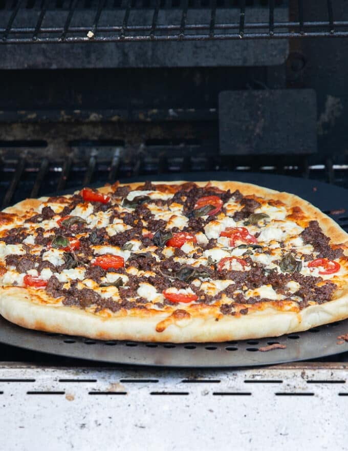 After grilling the pizza with the lid off, the lid is opened showing the golden crust and perfectly cooked grilled pizza. 