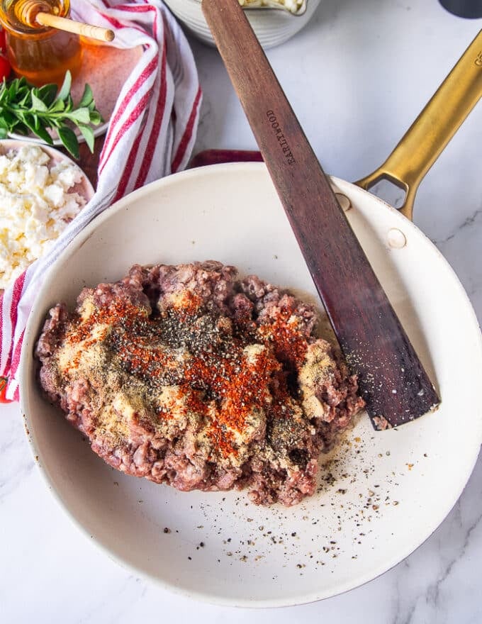 sausage ingredients all added in one skillet including the ground meat, spices and a wooden spoon mixing them