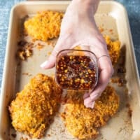 The baked chicken tenders ready and out of the oven golden and crispy, and a hand holding some hot honey ready to pour over
