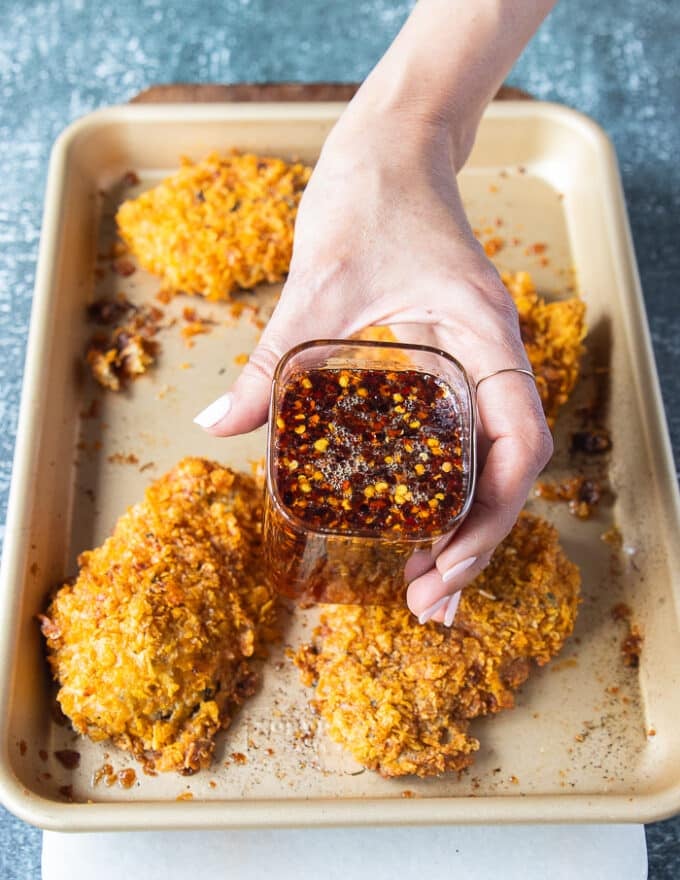 The baked chicken tenders ready and out of the oven golden and crispy, and a hand holding some hot honey ready to pour over 