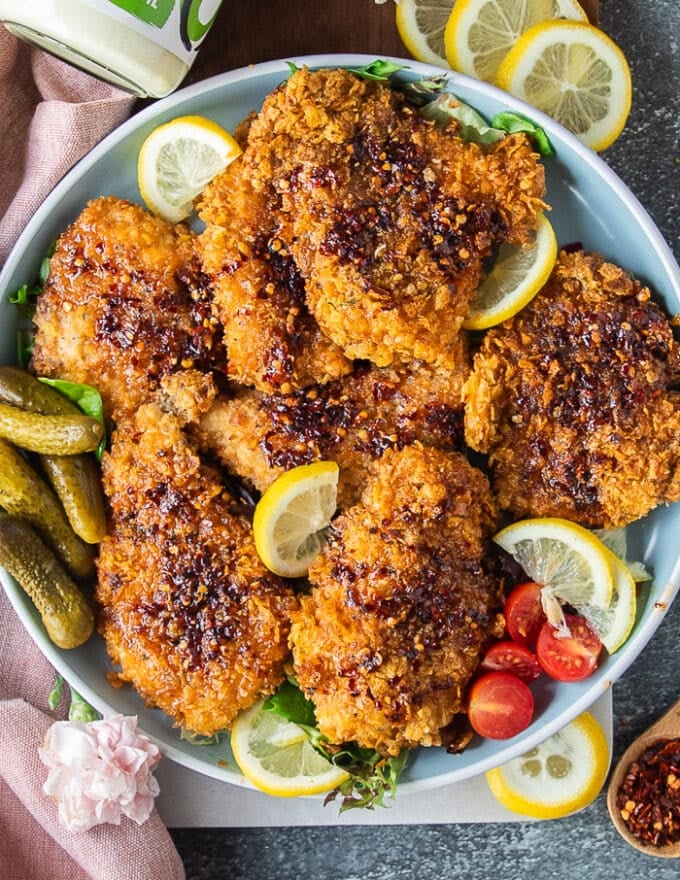 A plate of hot honey chicken dressed up with hot honey and surrounded by lemon slices 