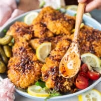 the hot honey chicken tenders arranged in a plate and hand pouring in a spoonful of hot honey on top