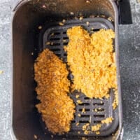 chicken tenders with cornflakes coating in an air fryer basked sprayed with oil ready to air fry
