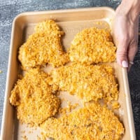 The coated chicken tenders all coated and arranged in a single layer on a baking sheet sprayed with oil ready to bake
