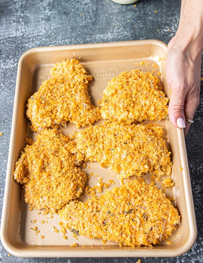 The coated chicken tenders all coated and arranged in a single layer on a baking sheet sprayed with oil ready to bake 