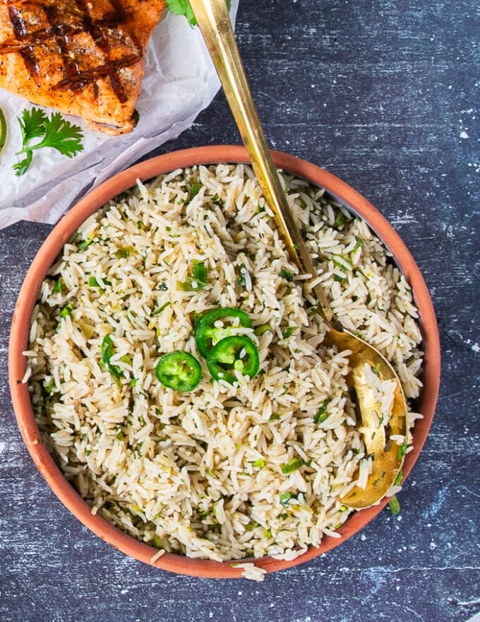 cilantro lime rice served on a plate with some jalapeno slices as a granish showing the specks of green on the fluffy rice 