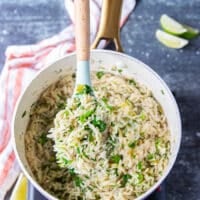 A spatula showing a spoonful of cilantro lime rice in the pot or rice cooker when tossed with the final lime zest, lime juice, cilantro , jalapeno and scallions showing specks of green and fluffy cooked white rice