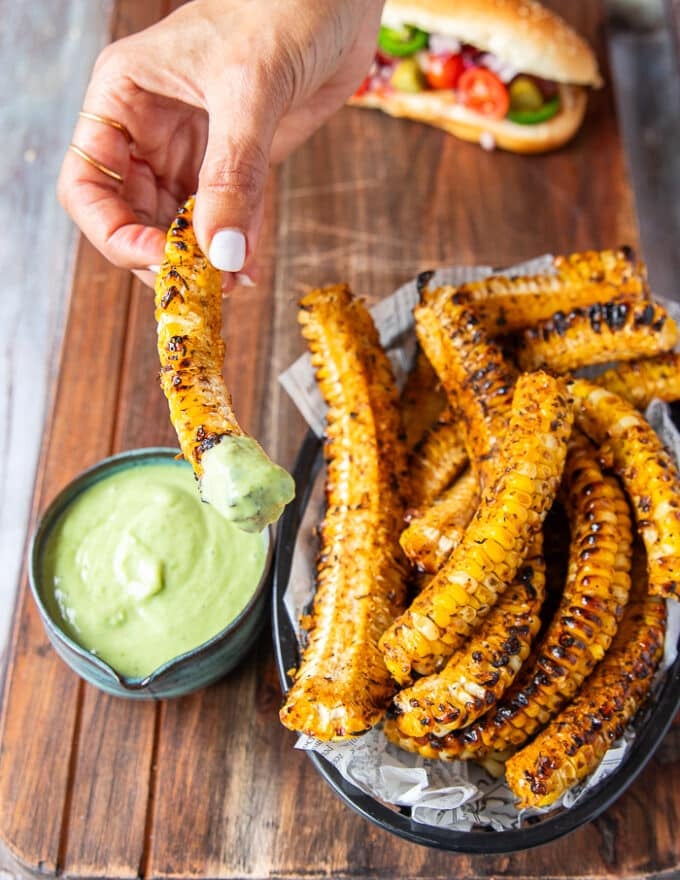 A hand holding a piece of seasoned corn ribs dipped into the avocado jalapeno sauce and showing close up of the dip 