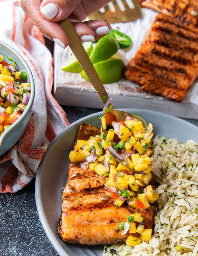 A hand spooning some mango pico de gallo over some grilled salmon fillets