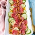 tuna crudo on a plate with sliced cucumbers, a citrus dressing, capers , lots of olive oil and fried garlic