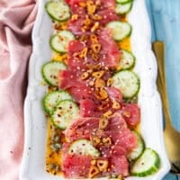 tuna crudo on a plate with sliced cucumbers, a citrus dressing, capers , lots of olive oil and fried garlic