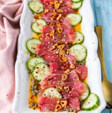 tuna crudo on a plate with sliced cucumbers, a citrus dressing, capers , lots of olive oil and fried garlic
