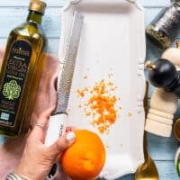 A hand zesting in an orange into the serving plate to make the vinaigrette for tuna crudo