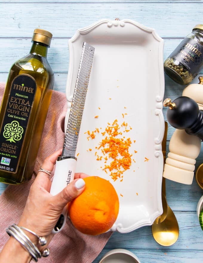 A hand zesting in an orange into the serving plate to make the vinaigrette for tuna crudo 
