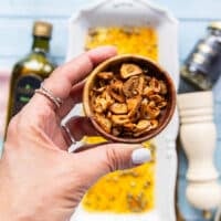 A hand holding a small bowl of golden toasted garlic chips ready to garnish the tuna crudo