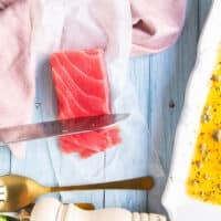 A hand holding a sharp knife thinly slicing the saku tuna into thin slices for the tuna crudo