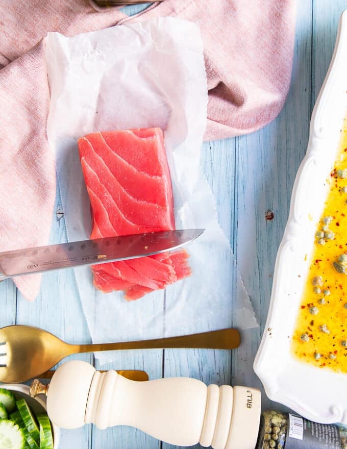 A hand holding a sharp knife thinly slicing the saku tuna into thin slices for the tuna crudo 
