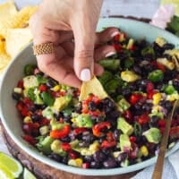 A hand holding a tortilla chip and scooping up some black bean and corn salad showing close up of the salad ingredients