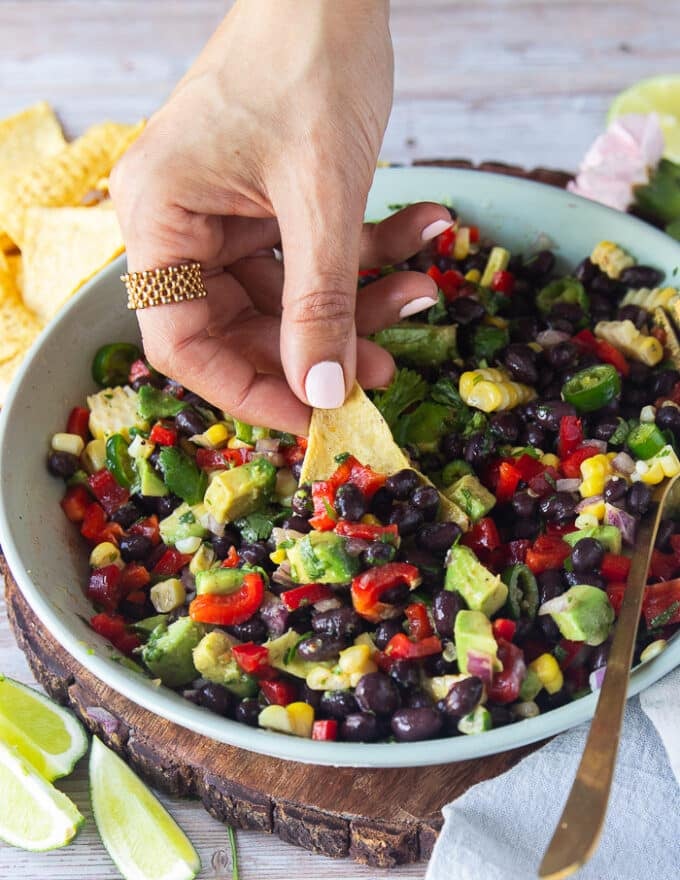 A hand holding a tortilla chip and scooping up some black bean and corn salad showing close up of the salad ingredients