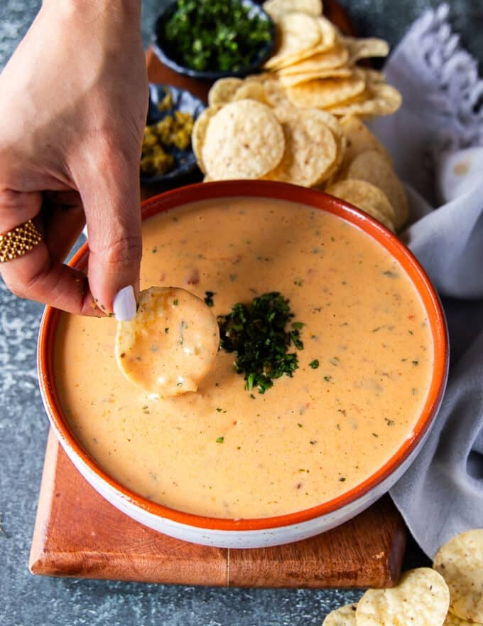 Close up of a hand scooping some queso with a tortilla chip showing the luscious texture of the dip