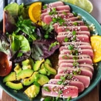 the tuna slices arranged over the ponzu sauce surroounde dby some avocado slices, garnished with scallions and sesame seeds and ready to serve