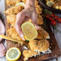 A hand squeezing lemon over perch fish right out of the oven