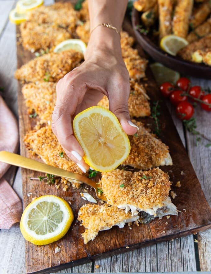 A hand squeezing lemon over perch fish right out of the oven 