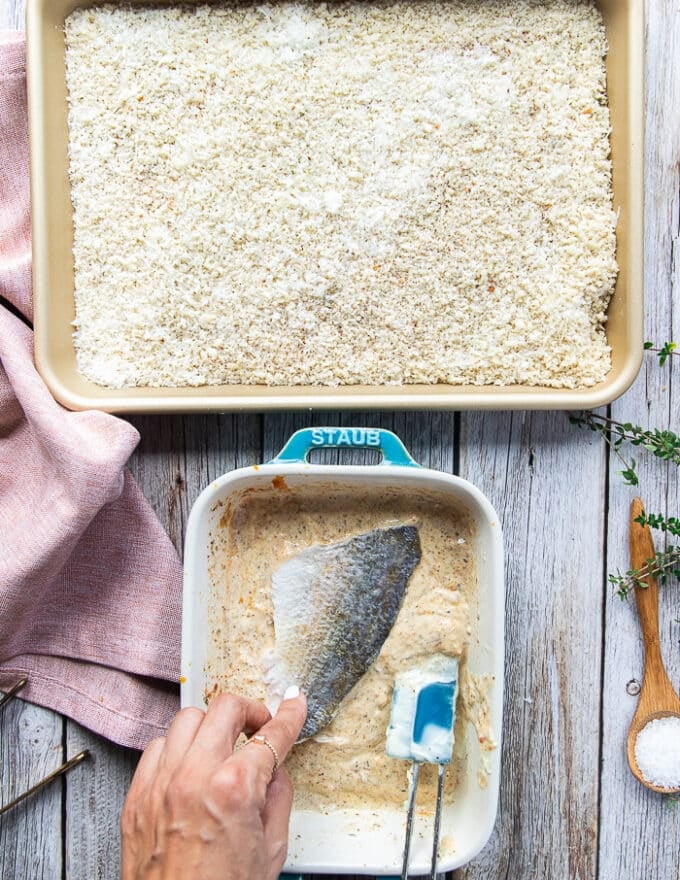 A hand dipping a piece of perch fish into the wet ingredients plate