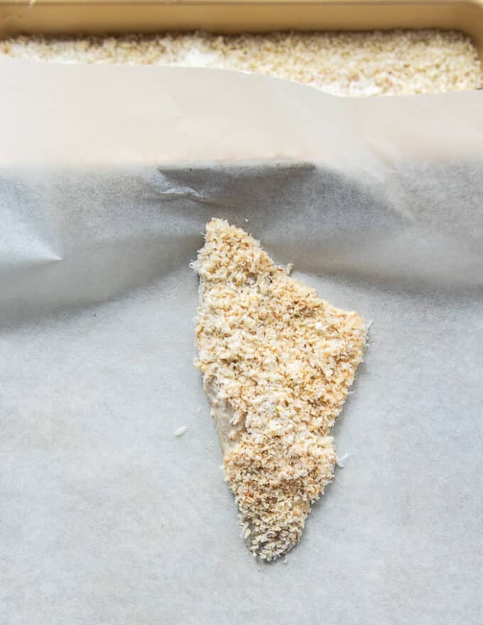 Fully coated perch fish placed on a parchment lined baking sheet 