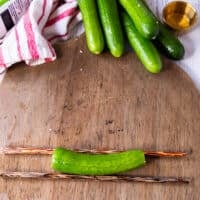 A cucumber is placed on top of two chopsticks on a cutting board