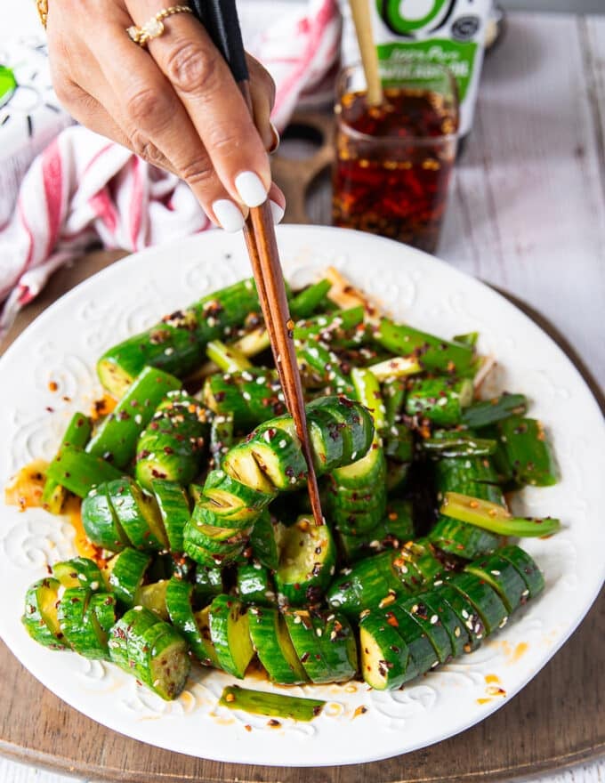 A hand holding two chopsticks and eating the Asian cucumber salad showing the spiral cucumbers dressed up 