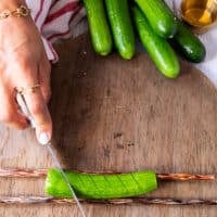 A hand holding a paring knife and making slits along the cucumber 1/4 inch apart on a 45 degree angle