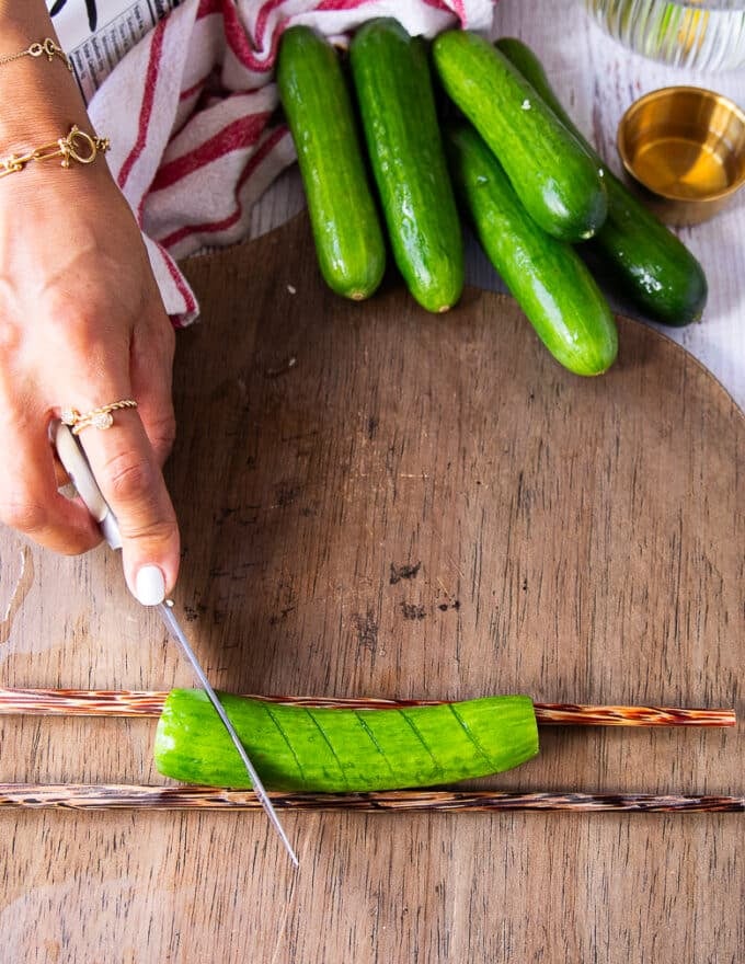 A hand holding a paring knife and making slits along the cucumber 1/4 inch apart on a 45 degree angle 