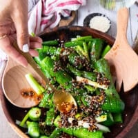 A hand pouring the chili oil and remaining ingredients over the cucumbers to make asian cucumber salad