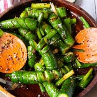 Tow spoons tossing the asian cucumber salad together with the dressing
