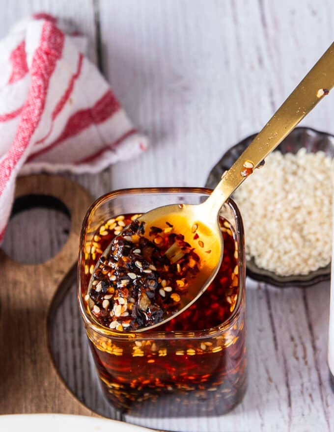 Close up of the chili oil recipe when mixed with a spoon showing the red hot oil infused with the chilli flakes and the bits of chillies, sesame , scallions, ginger, garlic within the oil 