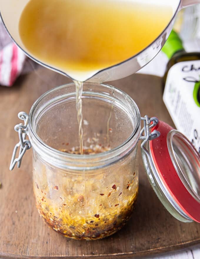 a hand pouring the hot oil carefully and slowly into the jar as it the oil begins ti bubble 