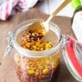 A spoon scooping some chili oil from a jar showing the chillies, garlic and all ingredients well blended into the oil