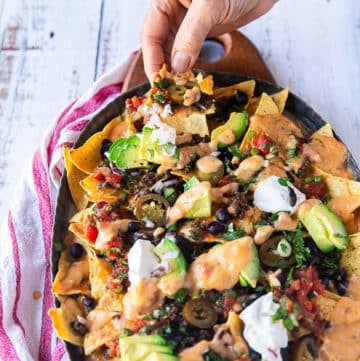 A hand pulling a nachos piece from the plate