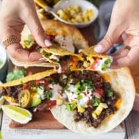 A hand pulling apart a ground beef taco showing the stretch of the cheese and toppings