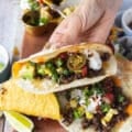 A hand holding a close up of a ground beef tacos showing the inside juicy beef melting cheese and all the topping like sour cream, salsa, cheesy sauce, guacamole and jalapeno