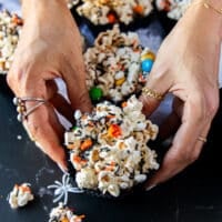 A hand holding a cup of halloween popcorn with some falling around it and a mini plastic skull surrounding the hand for a spooky feel