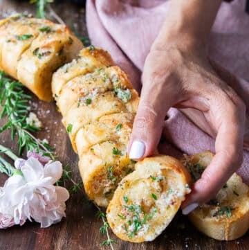 A hand holding one piece of air fryer garlic bread close up showing the texture and toppings